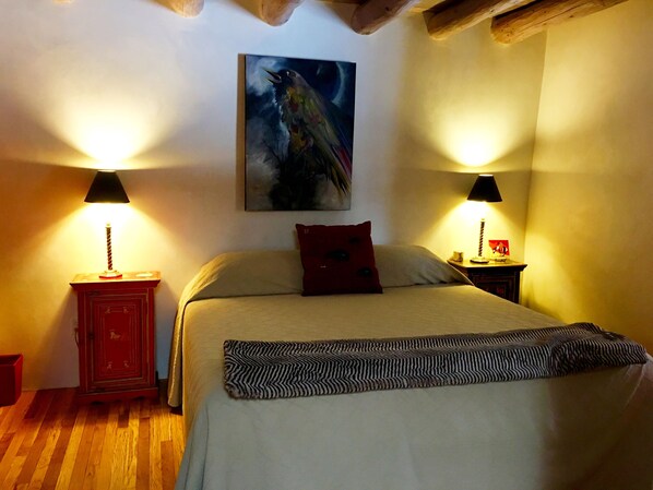 A bedroom with a bed, two bedside tables, a red cabinet, a painting on the wall, and two lamps.