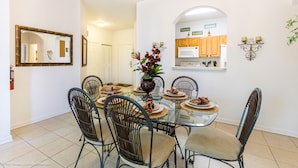 A dining area with a glass table surrounded by wicker chairs, a vase with flowers, and a kitchen visible through an archway. - Top floor on Disney's doorstep - Great location (Kissimmee)