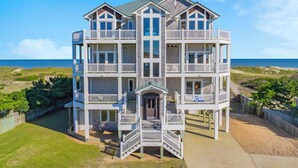 A multi-story beachfront property with balconies, a covered entrance, and a view of the ocean. - Premier Oceanfront Home with Pool, Hot Tub, Elevator, Game Room, and Theater (Waves)