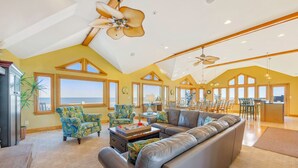 A spacious living room with a large sofa, patterned armchairs, and a dining area with a view of the ocean. - Premier Oceanfront Home with Pool, Hot Tub, Elevator, Game Room, and Theater (Waves)
