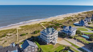 A coastal residential area with houses near the beach, featuring a large multi-story building with balconies and a swimming pool. - Premier Oceanfront Home with Pool, Hot Tub, Elevator, Game Room, and Theater (Waves)