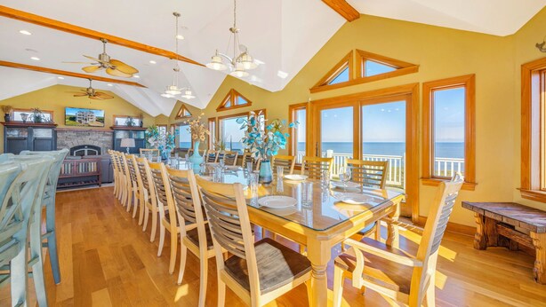 A spacious dining area with a large table and chairs, a fireplace, and a view of the ocean. - Premier Oceanfront Home with Pool, Hot Tub, Elevator, Game Room, and Theater (Waves)
