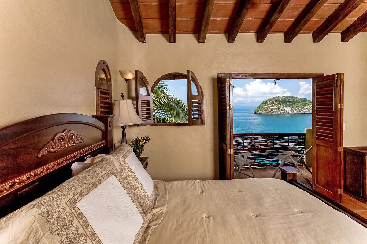 A bedroom with a bed, a nightstand, a lamp, and a view of the sea.