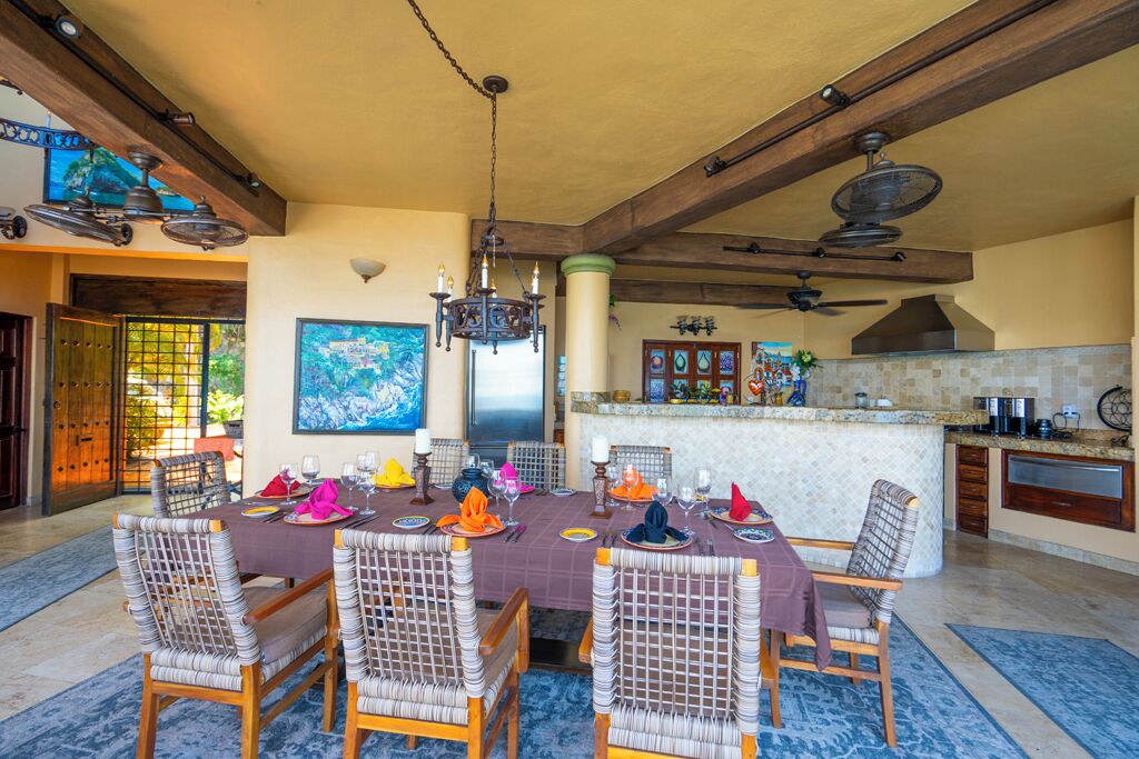 A dining area with a large table set for a meal, surrounded by wicker chairs.