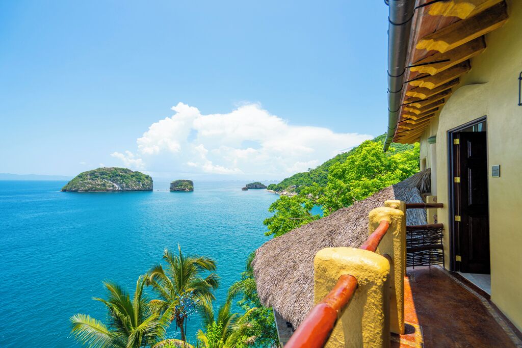 A coastal view with a thatched-roof building, a clear blue sea, and lush greenery.