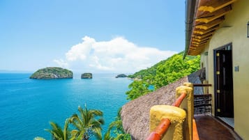 A coastal view with a thatched-roof building, a clear blue sea, and lush greenery.