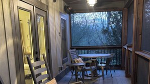 A covered porch with wooden flooring, rocking chairs, and a table with chairs.