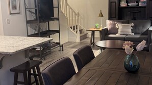 A dining area with a wooden table, chairs, a TV on a stand, a staircase, and a ceiling fan.
