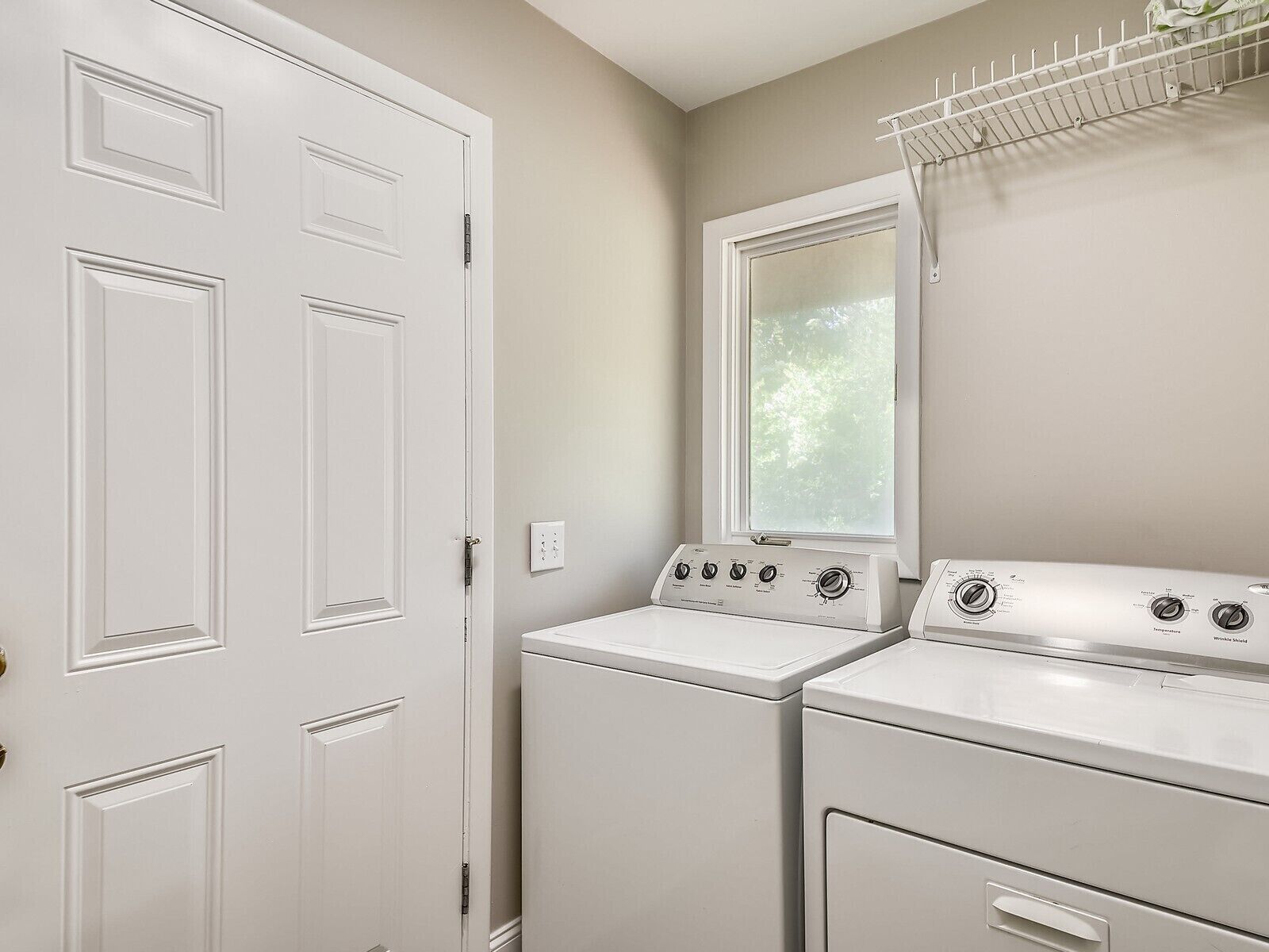 A laundry room with a white door, a window, and two stacked washers and dryers.