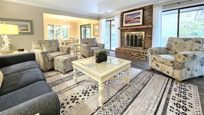 Un salón amplio con chimenea, asientos cómodos y ventanas grandes.