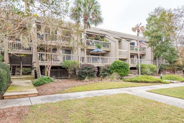 A multi-story residential building with balconies, a flag, and a well-maintained garden. - Seabrook Island Villa decorated with Charleston flair and Low Country Charm (Seabrook Island)