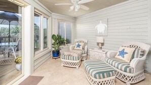 A sunlit room with wicker furniture, a ceiling fan, and a view of the outdoors.