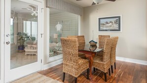 A dining area with wicker chairs, a glass-top table, and a ceiling fan.