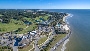 An aerial view of a coastal resort with a golf course, beachfront, and a large building complex.