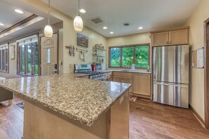 A modern kitchen with granite countertops, stainless steel appliances, and a large window overlooking a garden.