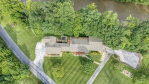 Ein großes Haus mit einem weitläufigen Garten, einer Auffahrt und einem Fluss im Hintergrund.