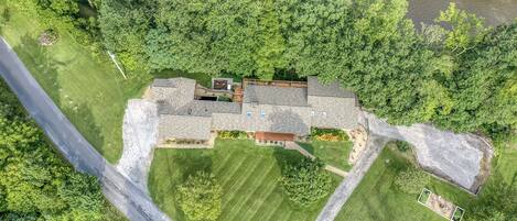 A large house with a spacious backyard, a driveway, and a river in the background.