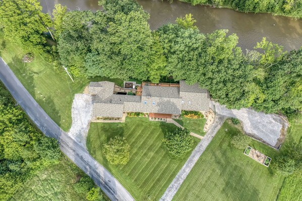 A large house with a spacious backyard, a driveway, and a river in the background.