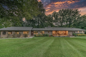 A single-story house with a well-maintained lawn, large windows, and a porch area.