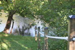 A wooden fence with a metal railing overlooking a body of water, surrounded by greenery.