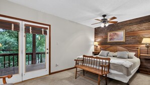 Ein Schlafzimmer mit Bett, einer Bank, einem Deckenventilator und Blick durch eine Tür auf eine Terrasse.