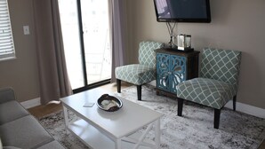 A living room with a white coffee table, two patterned armchairs, a blue cabinet, and a television mounted on the wall.