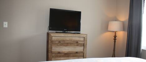 A bedroom with a bed, a wooden dresser, a television on top, and a lamp beside the window.