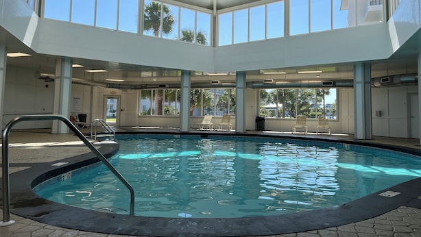 An indoor swimming pool with clear blue water, surrounded by lounge chairs and a covered area with large windows.