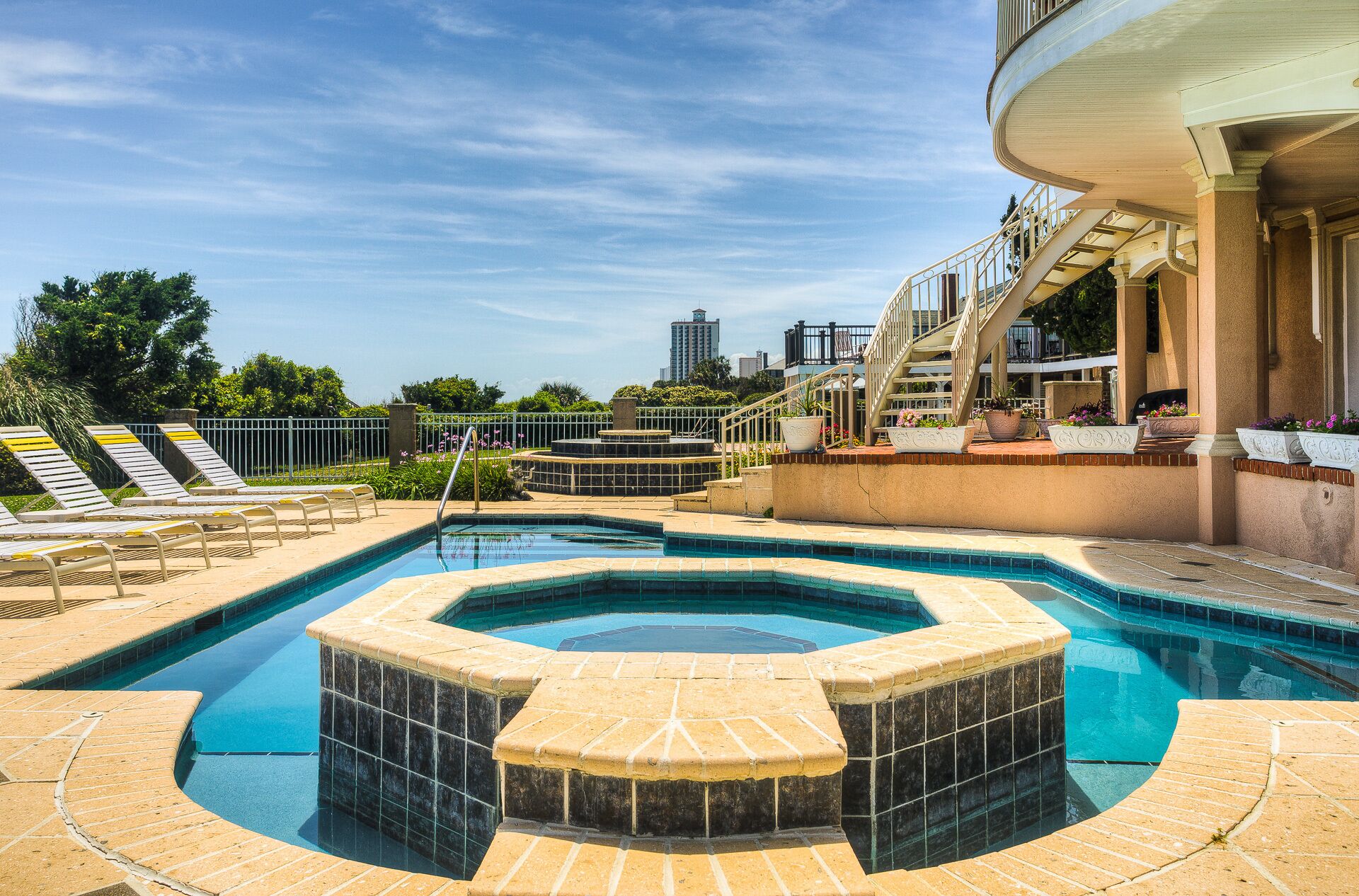 A swimming pool with a hot tub, sun loungers, and a staircase leading to an upper level.