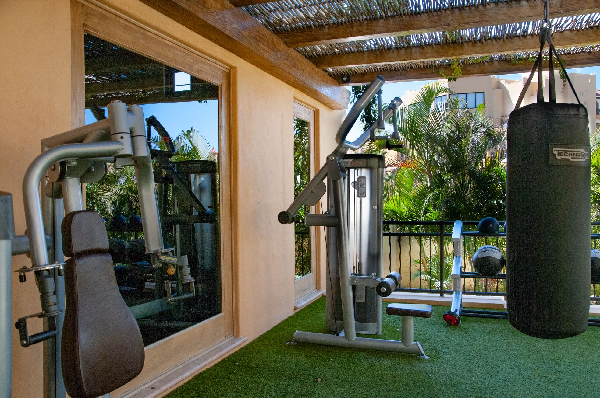 A gym with exercise equipment, a punching bag, and a view of palm trees and buildings.