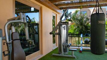 A gym with exercise equipment, a punching bag, and a view of palm trees and buildings.