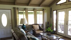Ein großzügiges Wohnzimmer mit Sofa, Sesseln und Couchtisch. Eine Tür mit Fenster, eine Lampe und ein Blumentopf sind ebenfalls vorhanden.