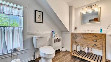 A bathroom with a toilet, a window with curtains, a sink with a mirror, and a wooden vanity.