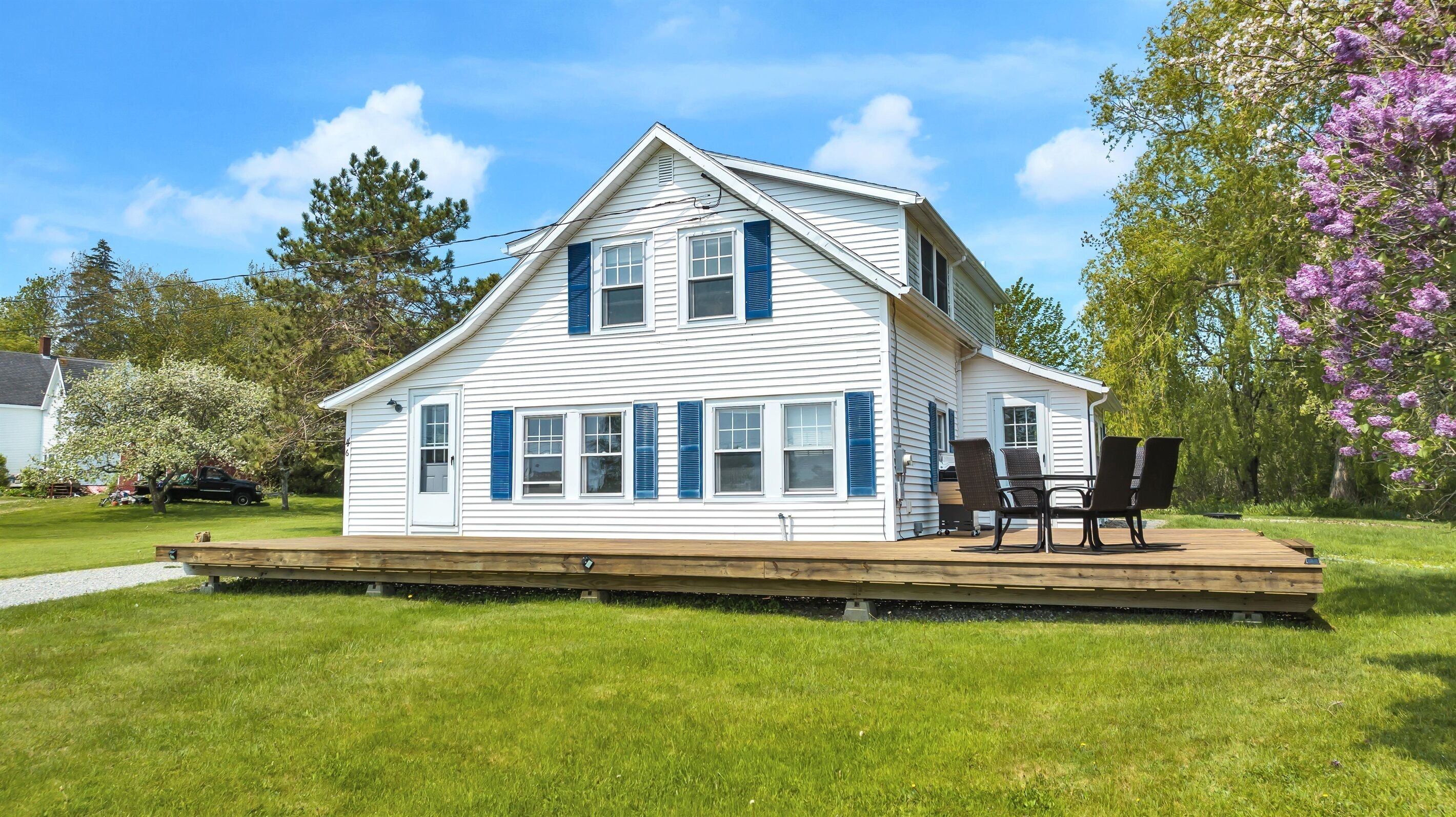 A white house with blue shutters, a deck, and a patio with chairs.