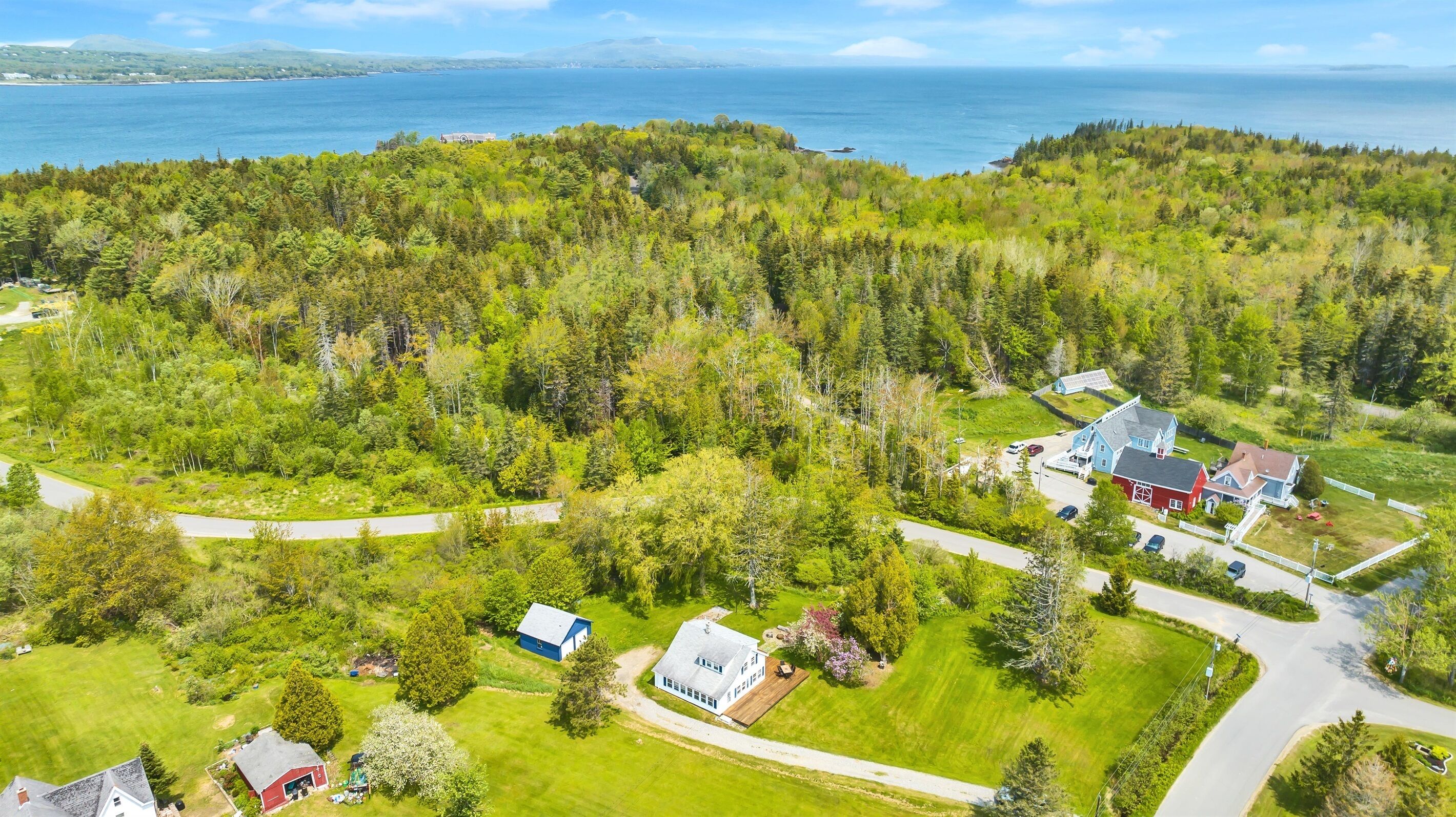 An aerial view of a residential area with houses, a road, and a body of water in the background.