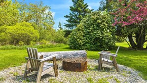 A wooden table and two chairs in a garden with a gravel path, surrounded by lush greenery and trees. - Harbor/🦞 Pound Access & Views from Large Deck (Owls Head)