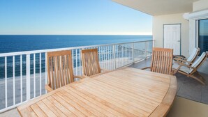 Un balcón con una mesa y sillas de madera, con vista a la playa y el océano.