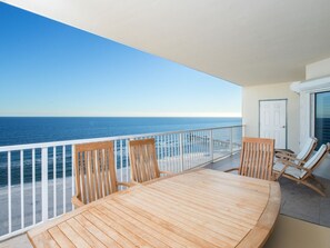 Un balcon avec une table et des chaises en bois, donnant sur une plage et l’océan.