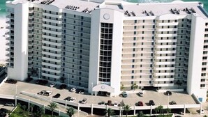 Un hotel de varios pisos con patio central, estacionamiento y vista al océano.