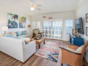 A living room with a white sofa, wicker chairs, a coffee table, and artwork on the walls.