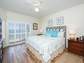 A bedroom with a bed, a ceiling fan, a nightstand, a dresser, and a window with shutters.