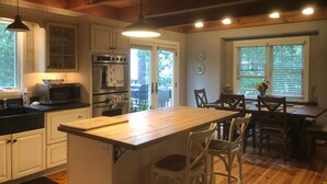 Una cucina con mobili in legno, un forno a microonde, un forno, una zona pranzo con tavolo e sedie, e un'ampia finestra.