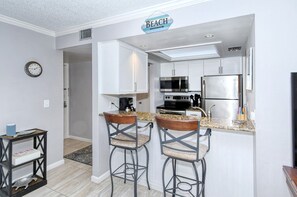 A kitchen with white cabinets, a microwave, a refrigerator, and two bar stools. - Firethorn 822- 2 bedrooms 1.5 baths overlooking canal w/private beach access (Siesta Key)
