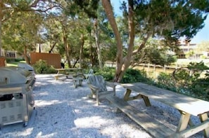 A picnic area with benches and a grill, surrounded by trees and a fence. - Firethorn 822- 2 bedrooms 1.5 baths overlooking canal w/private beach access (Siesta Key)