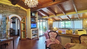Un interior rústico con paredes de piedra, vigas de madera, una araña, un televisor y muebles antiguos.