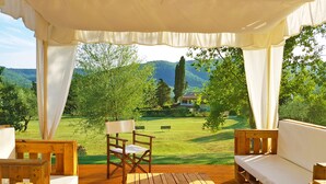Una terraza de madera con toldo blanco, una silla de madera y un banco.