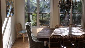 A dining area with a large wooden table and wicker chairs, large windows with a view of trees, and a chandelier. - Gorgeous Home 5 minute walk to beach (Kiawah Island)