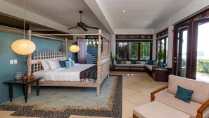 Ein Schlafzimmer mit einem Himmelbett, einem Deckenventilator und Blick ins Freie durch große Fenster.