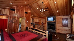 A log cabin interior with a bed, a fireplace, a television, and a kitchen area. - Lucky Log (Broken Bow)