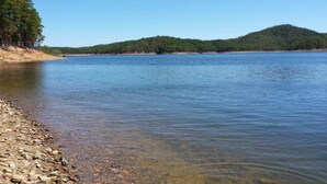 A calm lake with a rocky shoreline and forested hills in the background. - Lucky Log (Broken Bow)